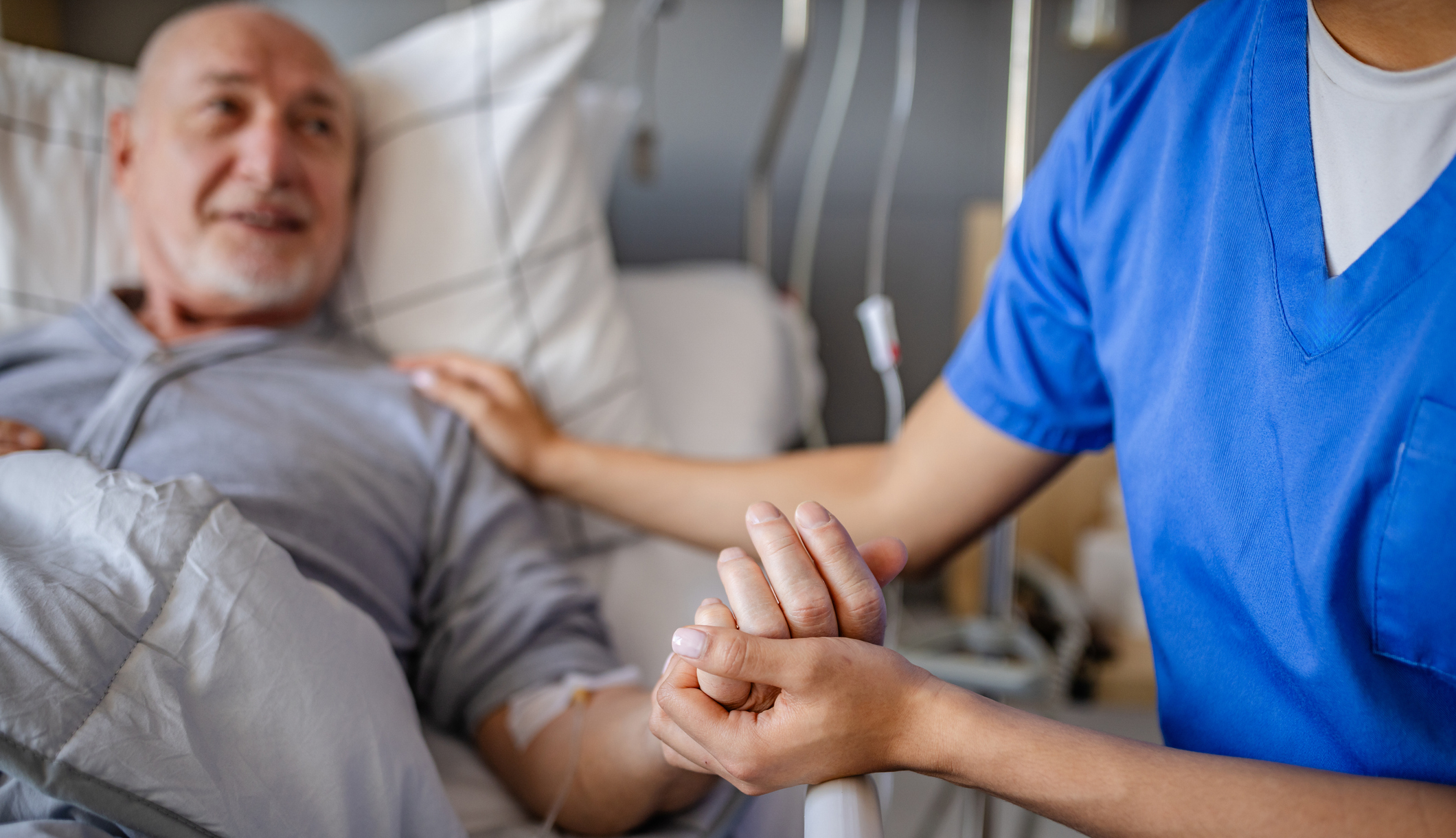 Senior man receives compassionate care from healthcare worker in hospital bed during recovery process